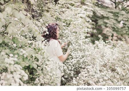 Woman spirea flowers. Portrait of a curly happy woman in a flowering bush with white spirea flowers. 105099757