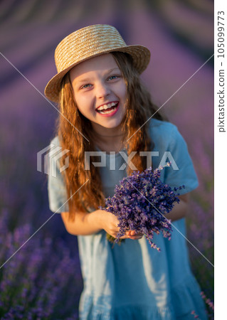 Lavender sunset girl. A laughing girl in a blue dress with flowing hair in a hat walks through a lilac field, holds a bouquet of lavender in her hands. Lavender sunset girl. A laughing girl in a blue dress with flowing hair in a hat walks through a lilac field, holds a bouquet of lavender in her hands. 105099773