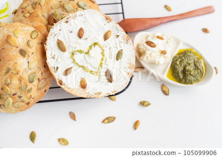 Freshly baked bagel with Philadelphia cheese, sunflower seeds and a painted heart with pesto sauce. Delicious and healthy breakfast. Freshly baked bagel with Philadelphia cheese, sunflower seeds and a painted heart with pesto sauce. Delicious and healthy breakfast. 105099906