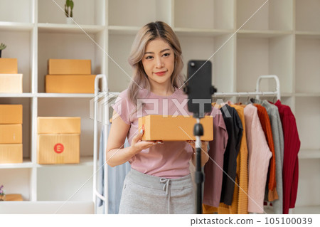 Asian beautiful woman sell clothes online live streaming at home. Young female use mobile phone video call shows goods to customer and present detail. Remote buying and purchase shopping concept Asian beautiful woman sell clothes online live streaming at home. Young female use mobile phone video call shows goods to customer and present detail. Remote buying and purchase shopping concept 105100039