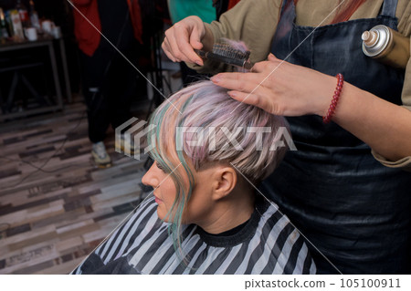 The hands of a professional girl in a salon comb the hair of a client of an adult woman with a stylish, fashionable hairstyle colored bob coloring 105100911