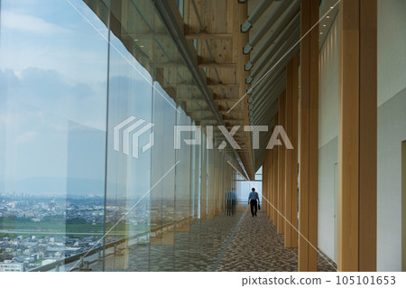 A man walks through a corridor surrounded by large glass windows of a skyscraper 105101653