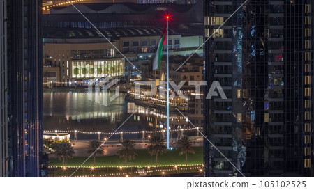Aerial view of Dubai Fountain in downtown with palms in park next to shopping mall and souq night to day timelapse, UAE 105102525