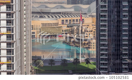 Aerial view of Dubai Fountain in downtown with palms in park next to shopping mall and souq timelapse, UAE 105102581