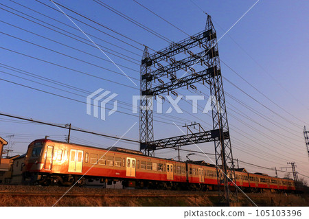 A red train on the Seibu Tamagawa Line running in the evening sun 105103396