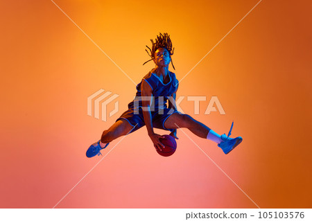 Dynamic image of athletic young man, basketball player in motion, jumping with ball against orange background in neon lights Dynamic image of athletic young man, basketball player in motion, jumping with ball against orange background in neon lights 105103576