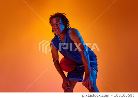 Competitive spirit. Young motivated man, athlete, basketball player standing with ball against orange background in neon lights 105103595