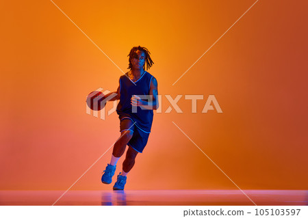 Young athletic man, basketball player in motion during game, training against orange background in neon lights 105103597