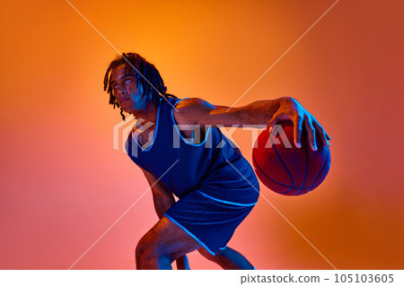Young athletic man, basketball player in motion during game, training against orange background in neon lights Young athletic man, basketball player in motion during game, training against orange background in neon lights 105103605