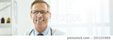 Cheerful male doctor sitting at the table with laptop in clinic 105103969