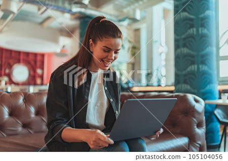 Smiling woman freelancer working on laptop while sitting on sofa in cozy coworking 105104056