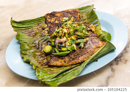 Grilled stingray fish with spices topped with okra vegetable on banana leaf popular food in Malaysia Grilled stingray fish with spices topped with okra vegetable on banana leaf popular food in Malaysia 105104225