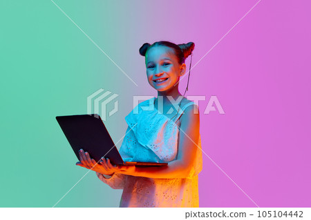 One smart, schoolage little girl, child posing with laptop against gradient pink-blue background. Online education, remote studying and leisure One smart, schoolage little girl, child posing with laptop against gradient pink-blue background. Online education, remote studying and leisure 105104442