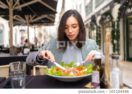 Portrait attractive woman in glasses eating salad at cafe table. 105104486