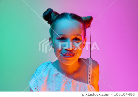 Charming beautiful little girl, child looking at camera with smile over gradient neon light background. 105104496