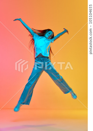 Active excited child wearing casual style clothes jumping high over neon light background. Concept of childhood, emotions, kids fashion 105104655