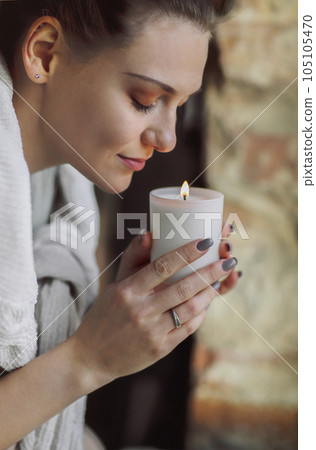 Young calm peaceful woman holding lit candle and smelling aroma 105105470