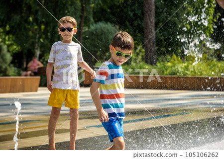 Boy having fun in water fountains. Child playing with a city fountain on hot summer day. Happy kids having fun in fountain. Summer weather. Active leisure, lifestyle and vacation Boy having fun in water fountains. Child playing with a city fountain on hot summer day. Happy kids having fun in fountain. Summer weather. Active leisure, lifestyle and vacation 105106262