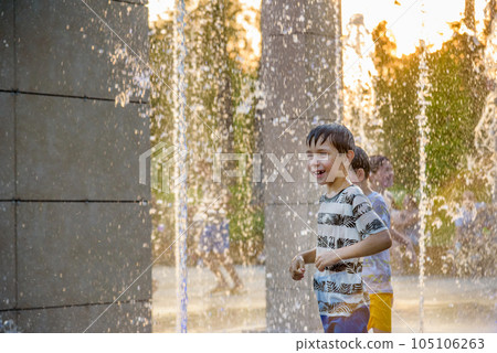 Boys jumping in water fountains. Children playing with a city fountain on hot summer day. Happy friends having fun in fountain. Summer weather. Friendship, lifestyle and vacation 105106263