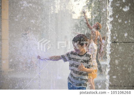 Boys jumping in water fountains. Children playing with a city fountain on hot summer day. Happy friends having fun in fountain. Summer weather. Friendship, lifestyle and vacation Boys jumping in water fountains. Children playing with a city fountain on hot summer day. Happy friends having fun in fountain. Summer weather. Friendship, lifestyle and vacation 105106268