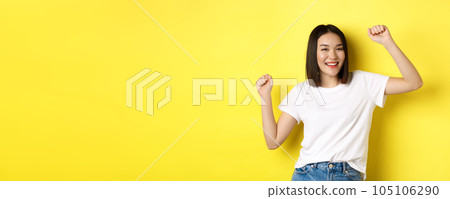 Carefree asian girl dancing and having fun, posing in white t-shirt against yellow background Carefree asian girl dancing and having fun, posing in white t-shirt against yellow background 105106290