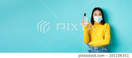 Covid-19, social distancing and pandemic concept. Cheerful asian woman showing hand sanitizer, recommend use antiseptic from coronavirus, wearing medical mask 105106351