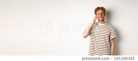 Hipster with red hair and glasses talking on mobile phone, smiling during conversation, white background 105106385