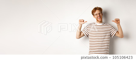 Cheerful and funny redhead man with beard, wearing glasses, laughing and pointing at himself, standing over white background 105106423