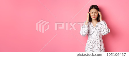 Image of upset asian woman having headache, feeling unwell or dizzy, close eyes and massaging head, suffering migraine, standing over pink background 105106437