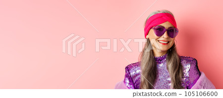 Fashion. Close up of stylish senior woman smiling happy at camera, wearing sunglasses and disco headband, pink background Fashion. Close up of stylish senior woman smiling happy at camera, wearing sunglasses and disco headband, pink background 105106600
