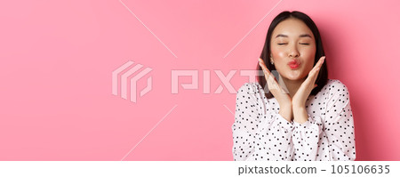 Beauty and skin care concept. Close-up of beautiful asian girl close eyes, pucker lips for kisses, showing cute perfect face, standing over pink background 105106635
