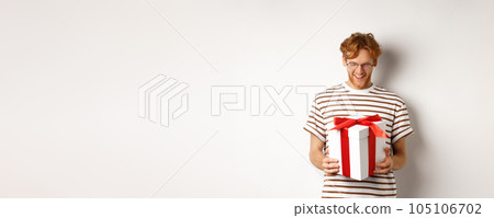 Valentines day and holidays concept. Happy bearded guy holding his gift and smiling, looking at box with present inside, standing over white background Valentines day and holidays concept. Happy bearded guy holding his gift and smiling, looking at box with present inside, standing over white background 105106702