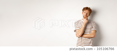Portrait of thoughtful man with red hair thinking, looking at upper left corner and making choice, standing over white background 105106766