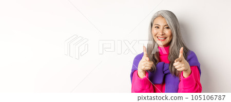 Beautiful and stylish asian grandmother pointing at camera, you can do this gesture, congratulating or praising, standing over white background 105106787
