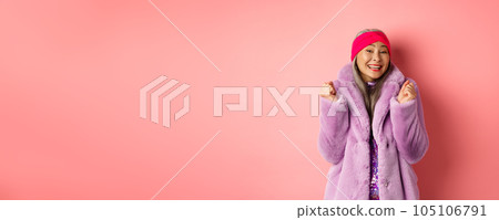 Cheerful asian lady in stylish funky coat, celebrating victory or success, saying yes and smiling happy, standing over pink background Cheerful asian lady in stylish funky coat, celebrating victory or success, saying yes and smiling happy, standing over pink background 105106791