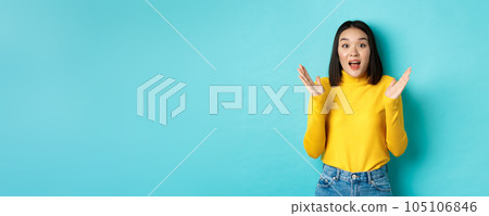 Image of happy asian woman clap hands and looking amazed, standing in yellow pullover over blue background 105106846