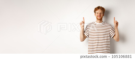 Smiling redhead guy with beard, pointing fingers up and showing advertisement, standing over white background Smiling redhead guy with beard, pointing fingers up and showing advertisement, standing over white background 105106881