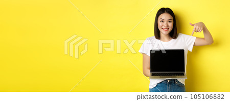 Young asian woman demonstrate online offer, showing laptop screen and smiling, standing over yellow background Young asian woman demonstrate online offer, showing laptop screen and smiling, standing over yellow background 105106882
