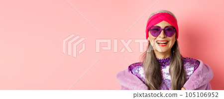 Fashion. Close up of stylish senior woman smiling happy at camera, wearing sunglasses and disco headband, pink background Fashion. Close up of stylish senior woman smiling happy at camera, wearing sunglasses and disco headband, pink background 105106952