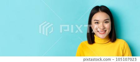 Beauty and skincare concept. Close up of smiling asian female model with perfect skin and white teeth, standing over blue background 105107023