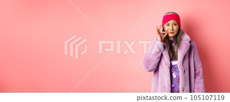 Fashion and shopping concept. Cunning asian senior woman in stylish clothes keeping secret, squinting and looking devious at camera, zipping mouth, making promise, pink background Fashion and shopping concept. Cunning asian senior woman in stylish clothes keeping secret, squinting and looking devious at camera, zipping mouth, making promise, pink background 105107119