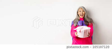 Surprised senior asian woman receiving valentines day gift and smiling amazed, holding present box, standing over white background Surprised senior asian woman receiving valentines day gift and smiling amazed, holding present box, standing over white background 105107120