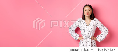 Beautiful asian woman in dress pucker lips and close eyes, waiting for kiss, standing over pink background Beautiful asian woman in dress pucker lips and close eyes, waiting for kiss, standing over pink background 105107187