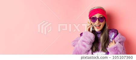 Fashion. Close-up of stylish asian senior woman hear amazing news on mobile phone, smiling happy at camera, wearing trendy sunglasses, pink background Fashion. Close-up of stylish asian senior woman hear amazing news on mobile phone, smiling happy at camera, wearing trendy sunglasses, pink background 105107360