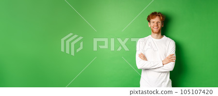 Young ambitious man with red hair standing over green background, holding hands crossed on chest and smiling Young ambitious man with red hair standing over green background, holding hands crossed on chest and smiling 105107420