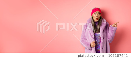 Cool asian granny pointing finger right and showing promo offer, checking out special deal on pink background Cool asian granny pointing finger right and showing promo offer, checking out special deal on pink background 105107441