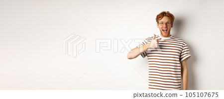 Amazed and fascinated redhead guy checking out something awesome, showing thumb-up and scream yes with joy, standing over white background Amazed and fascinated redhead guy checking out something awesome, showing thumb-up and scream yes with joy, standing over white background 105107675