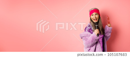 Gorgeous asian senior woman singing karaoke in mic, perform song and looking happy, standing over pink background Gorgeous asian senior woman singing karaoke in mic, perform song and looking happy, standing over pink background 105107683
