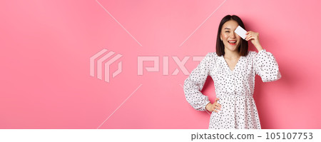 Shopping concept. Pretty asian woman holding bank credit card and smiling, standing over pink background Shopping concept. Pretty asian woman holding bank credit card and smiling, standing over pink background 105107753