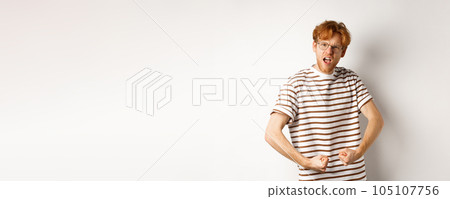 Image of confident and strong redhead man flexing biceps, showing muscles after gym, standing over white background 105107756